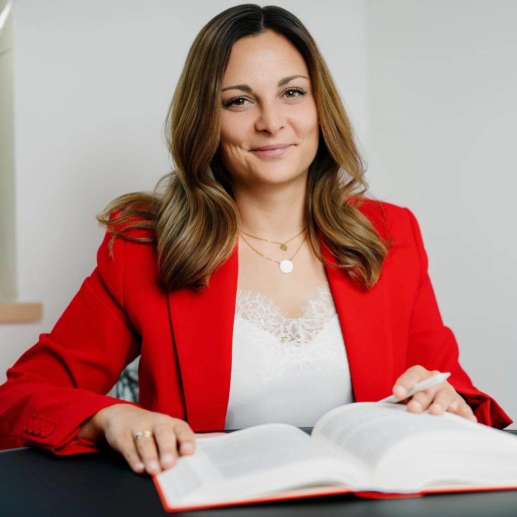 Patricia Bauer sitzt an einem Tisch vor einem aufgeschlagenem Gesetzbuch und lächelt